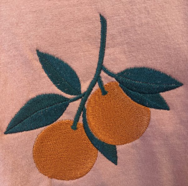 Embroidered oranges and leaves on a pink fabric background